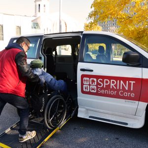 Senior in wheelchair is pushed into SPRINT Senior Care van by man in red vest.